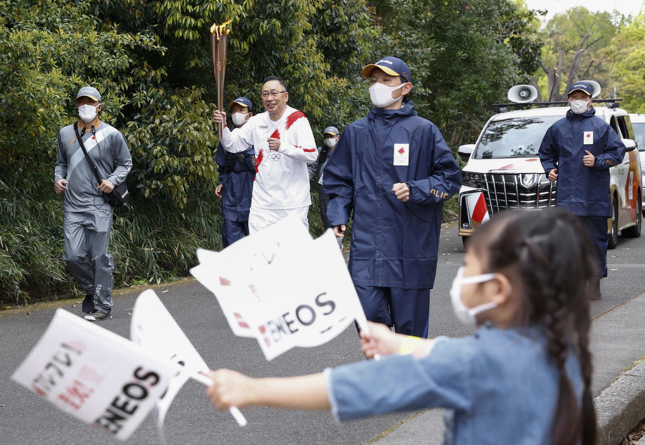 大阪府吹田市の万博記念公園で行われた聖火リレー。並走する関係者はマスクを着用した（共同）
