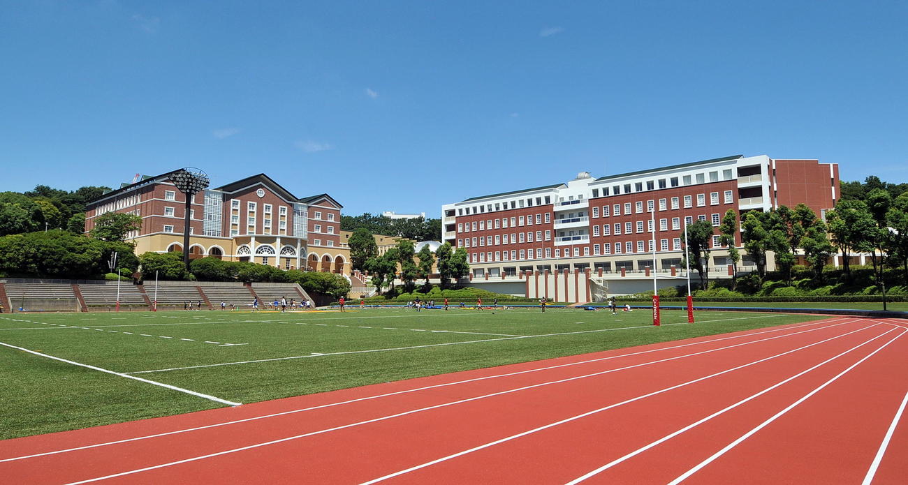 横浜市にある玉川学園キャンパスの記念グラウンドや高校校舎（奥左）、ホール（奥右）（玉川学園提供）