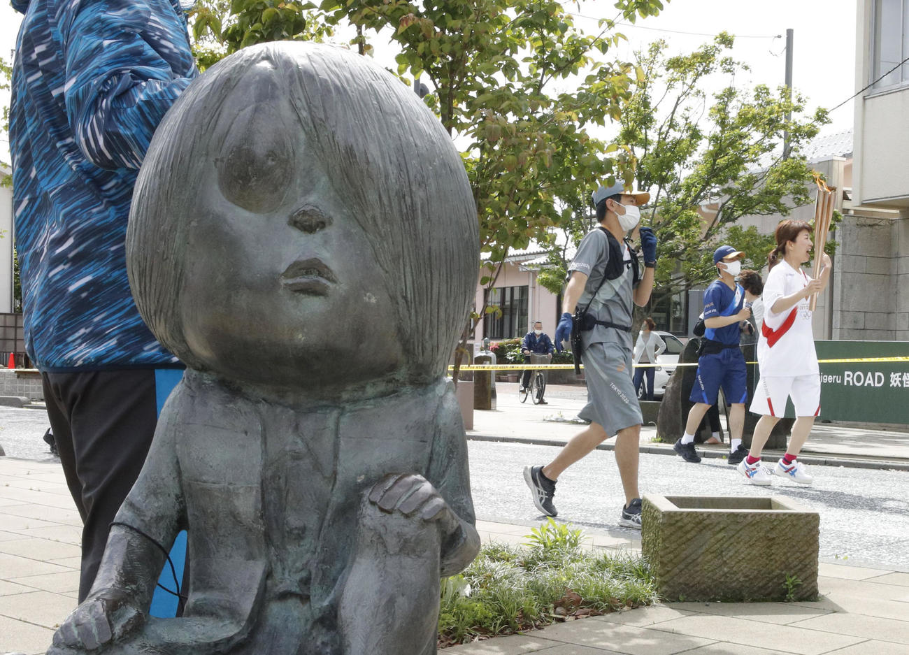 「水木しげるロード」を走る聖火ランナー。左は「鬼太郎」の像（共同）