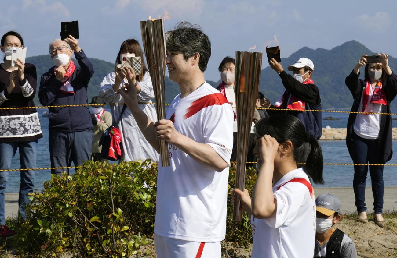 次走者とポーズをとる聖火ランナーの荻野正二さん（左）（共同）