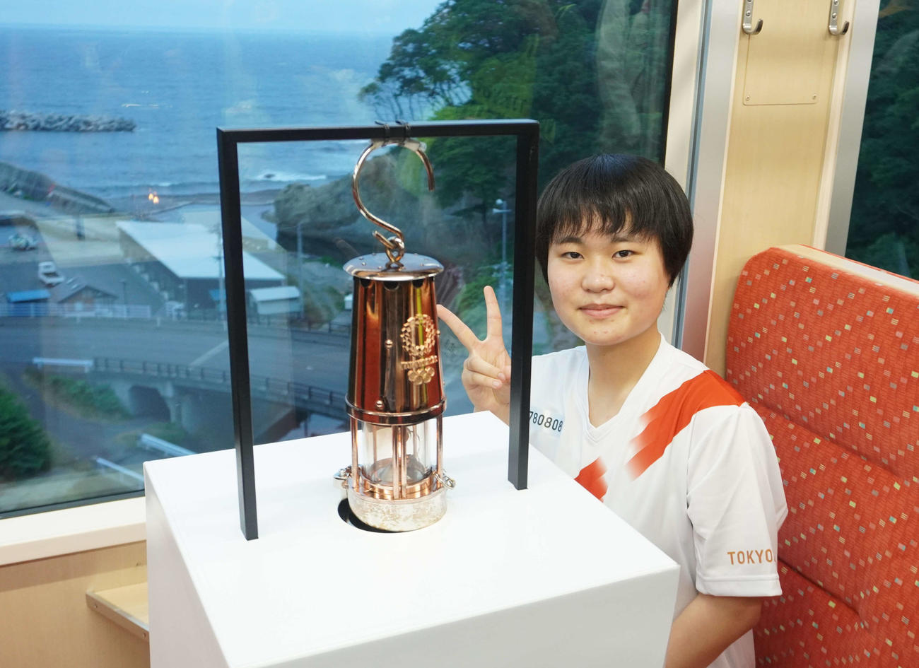 三陸鉄道の車内で聖火を前にピースをする金子恵美さん（撮影・沢田直人）