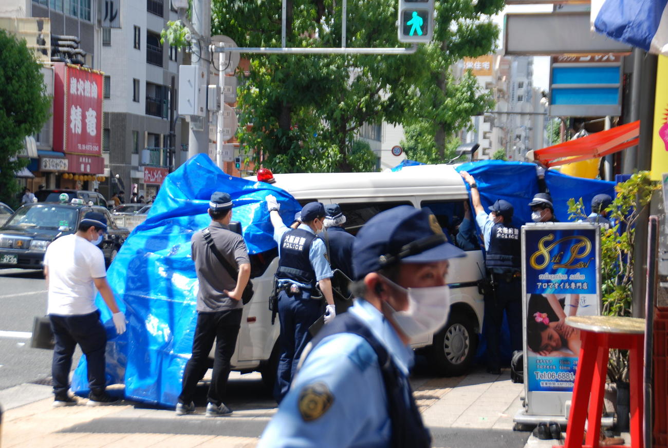 女性が倒れていたビルの前の捜査車両を青いシートで覆う大阪府警の捜査員ら（撮影・松浦隆司）