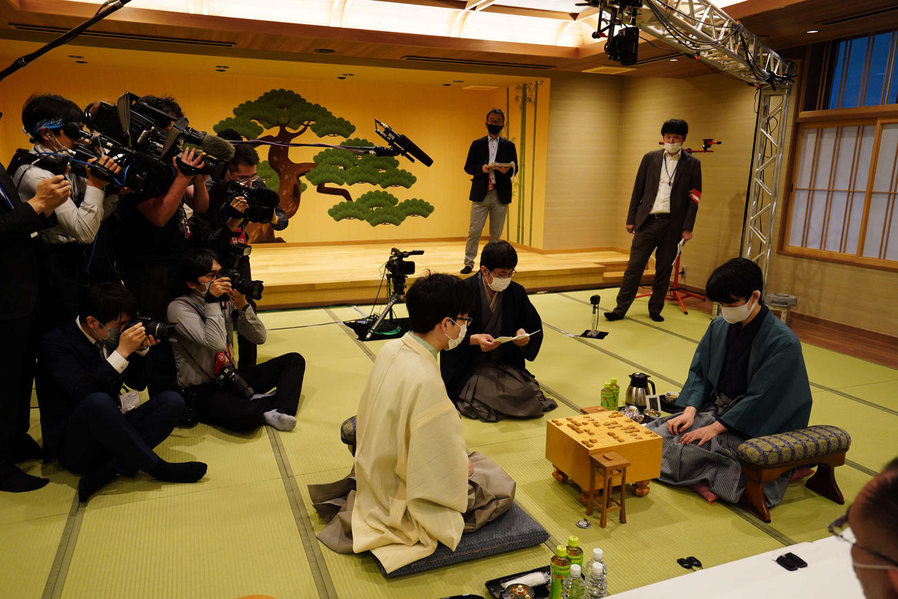 豊島将之竜王（左）対藤井聡太王位（右）の王位戦7番勝負第2局は立会人の広瀬章人八段（中央）が封じ手を開封して2日目が始まった（日本将棋連盟提供）