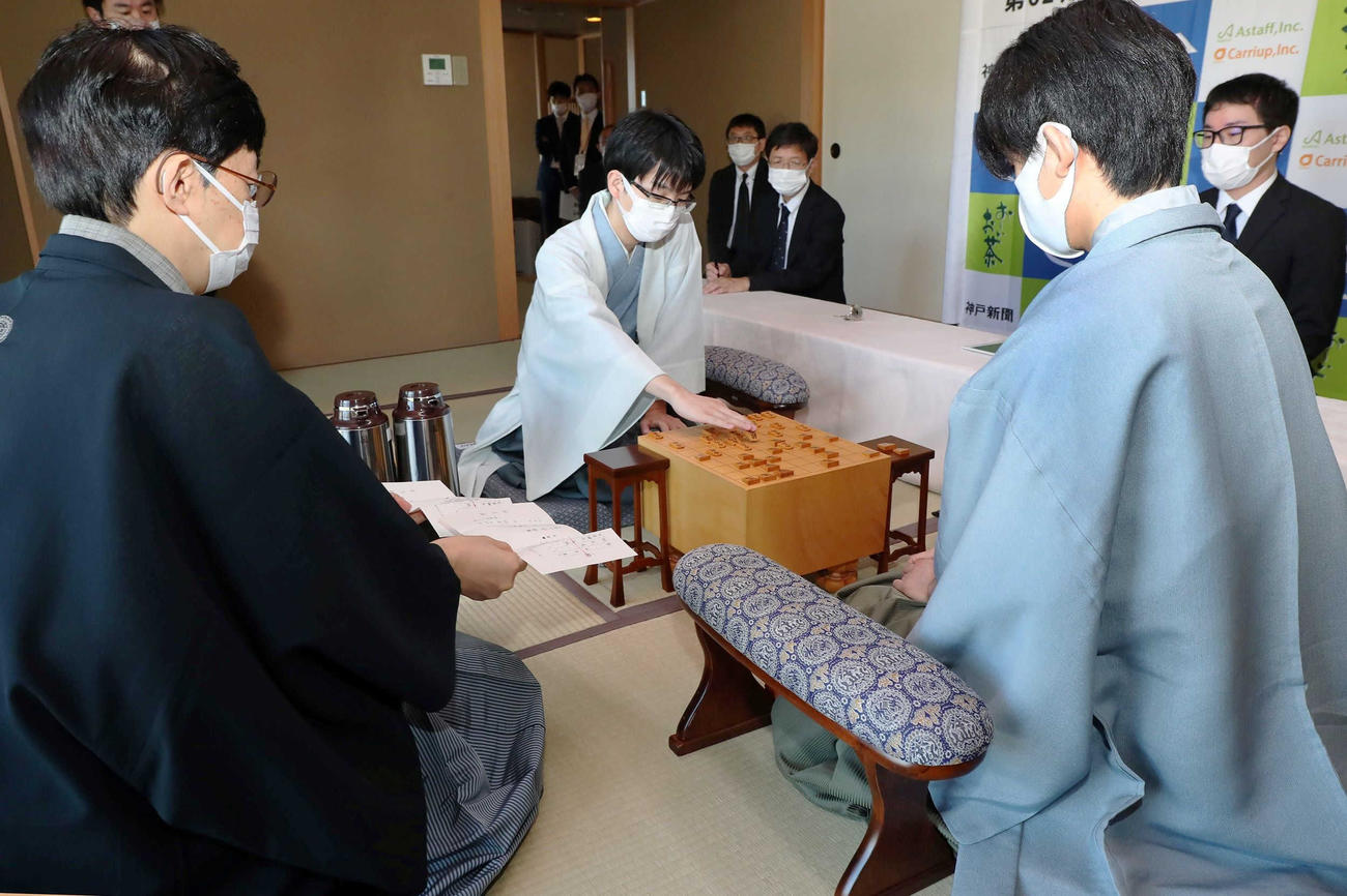 立会人の谷川浩司九段（左）が封じ手を示し、対局を再開する豊島将之竜王（中央奥）と藤井聡太王位