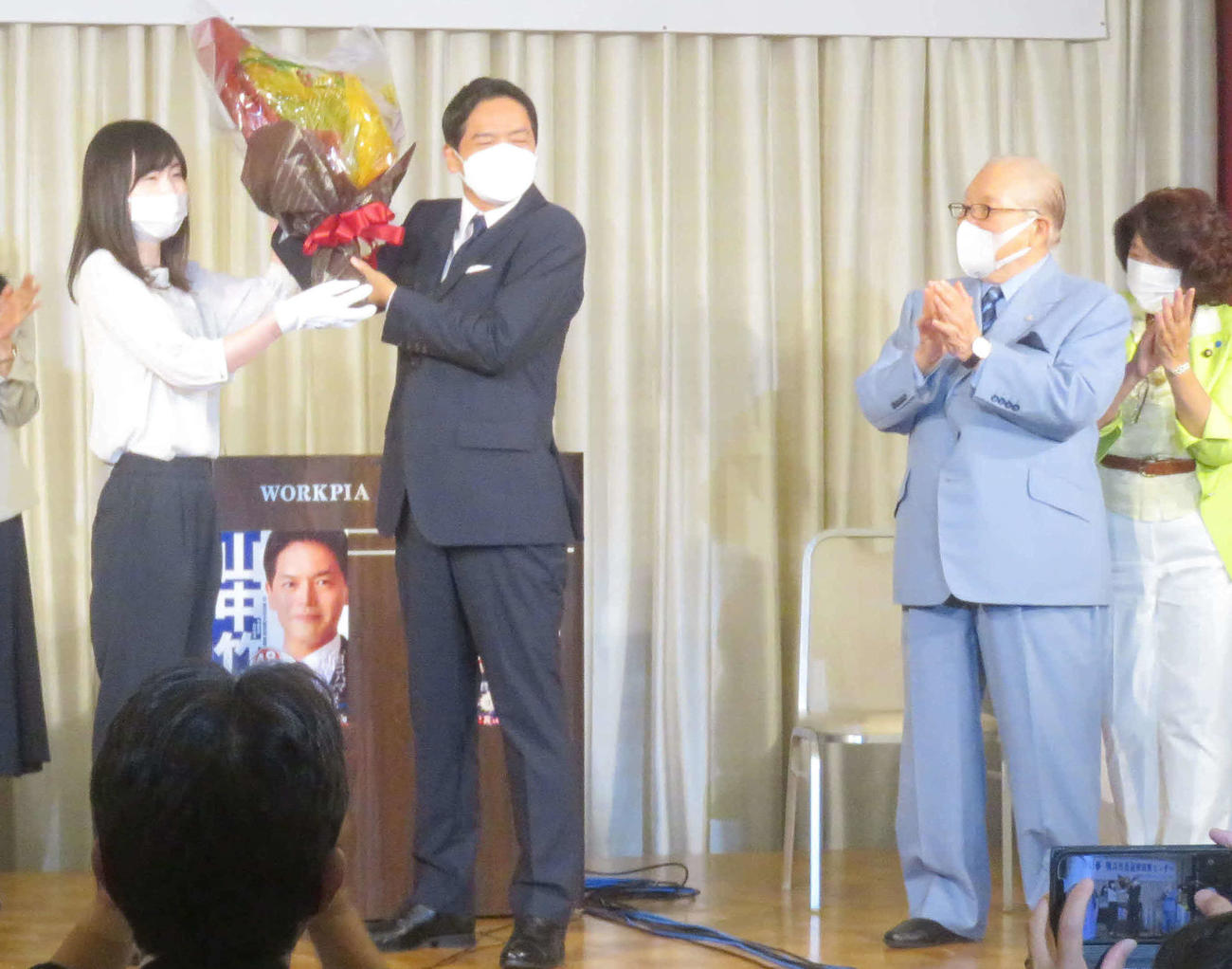 会見で花束を手にする山中竹春氏と、拍手する「ハマのドン」と呼ばれる藤木幸夫氏（右）（撮影・大上悟）