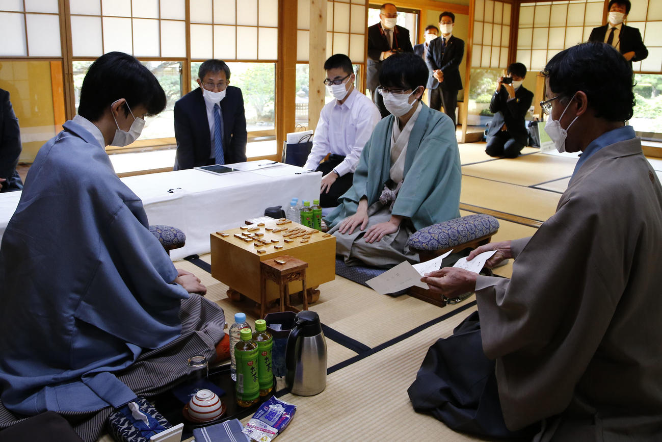 立会人の深浦康市九段（手前右）から豊島将之竜王（手前中央）の封じ手を示される藤井聡太王位（手前左）（代表撮影）