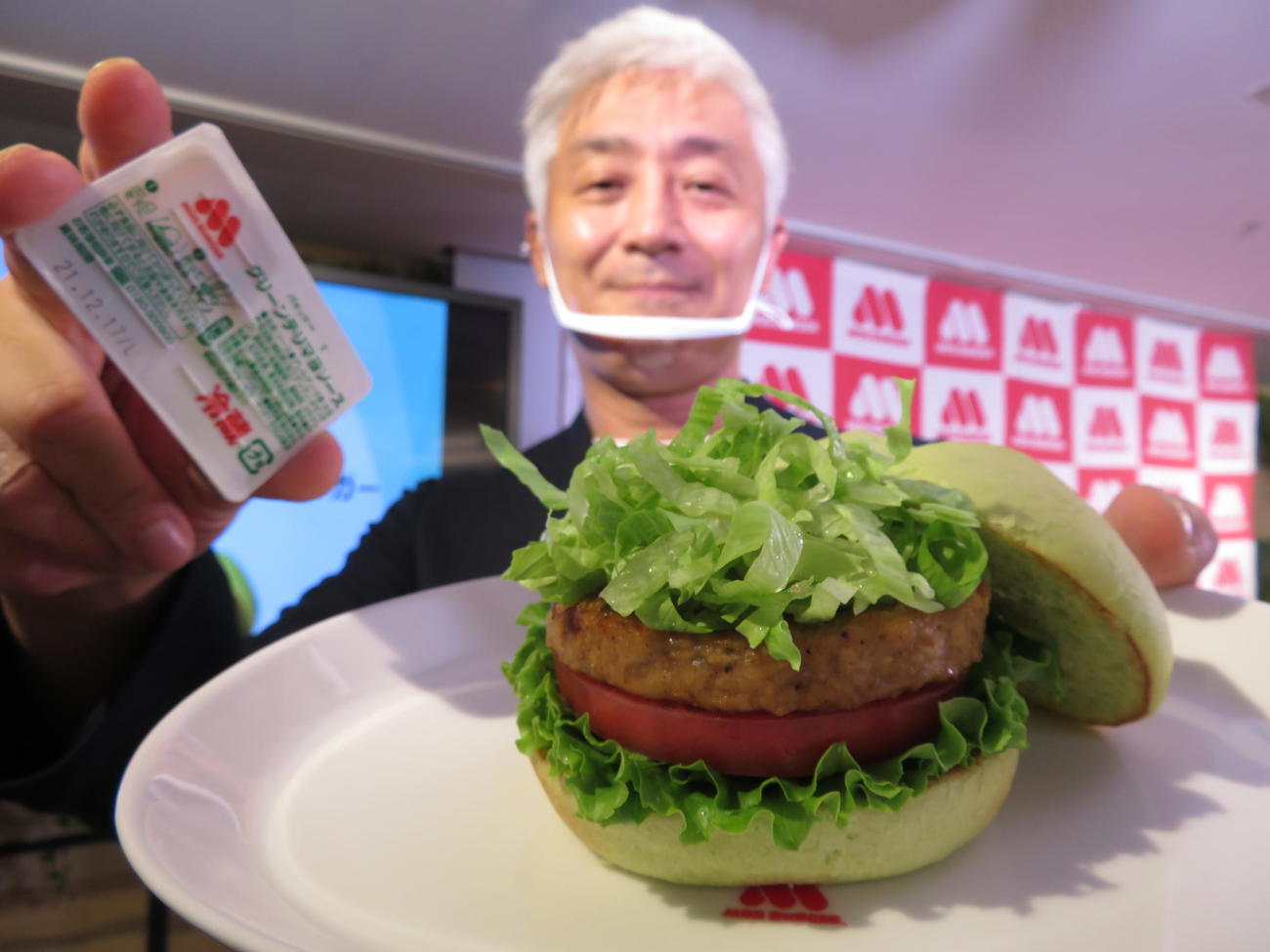 グリーンバーガー〈テリヤキ〉を担当したモスバーガー商品開発部長の濱崎真一郎さんは2種の付け足しソースの入ったパキッテを右手に持って笑顔をみせた