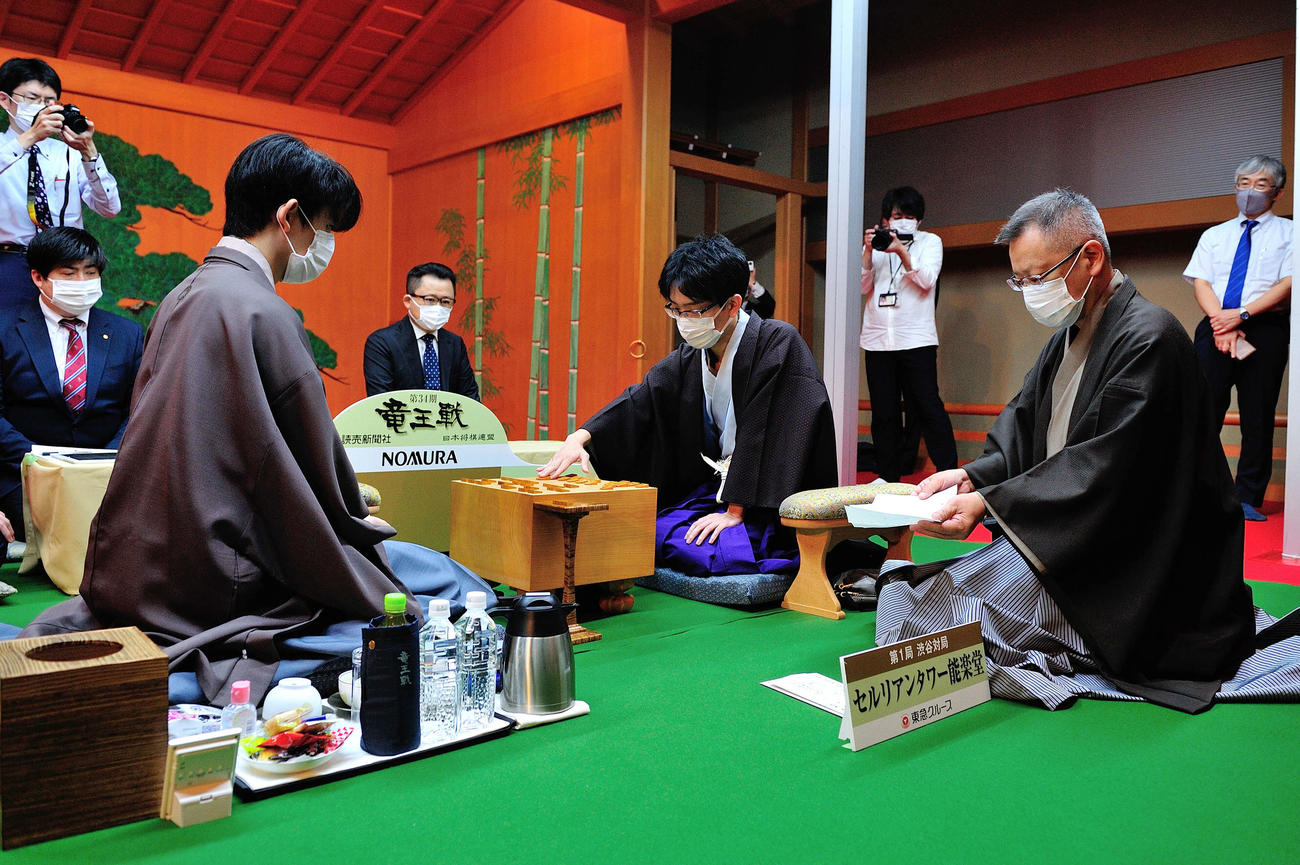 封じ手を開封した立会人の中村修九段（右）の指し手を見せる豊島将之竜王（中央）とそれを注視する藤井聡太3冠（左、日本将棋連盟提供）