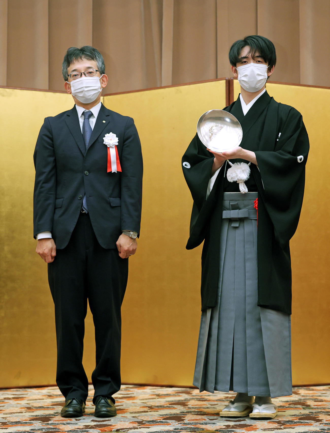 王位杯を手にする藤井聡太王位。左は日本将棋連盟の佐藤康光会長（代表撮影）