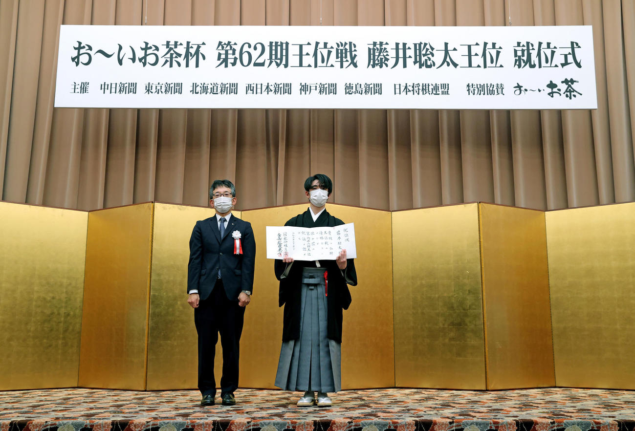 就位状を手にする藤井聡太王位。左は日本将棋連盟の佐藤康光会長（代表撮影）