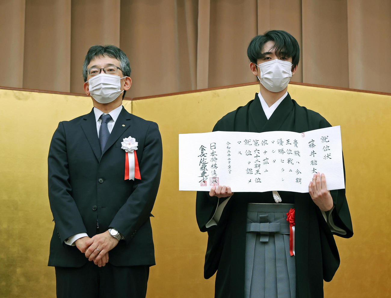 就位状を手にする藤井聡太王位。左は日本将棋連盟の佐藤康光会長（代表撮影）