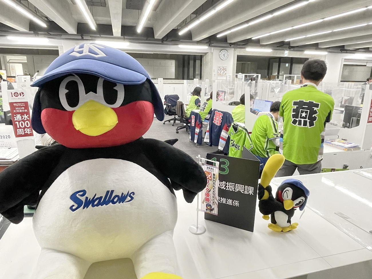 ヤクルトのユニホーム着用で業務を行って日本一を願う燕市の職員たち。燕市PR隊鳥を務めるつば九郎の人形も仁王立ち（燕市提供）