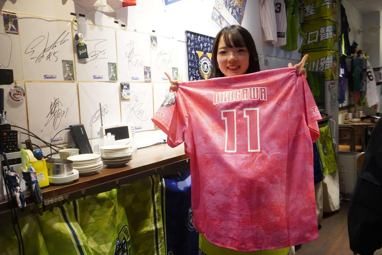 奥川恭伸のユニホームを持ち笑顔を見せる「ヤクルト推し　居酒屋　和’s」の店員大竹咲来さん（撮影・沢田直人）