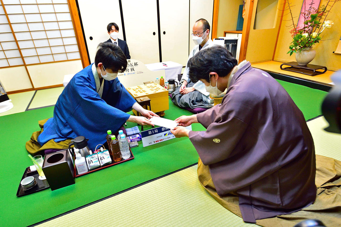 藤井竜王（左）は封じ手の封筒を立会人の森内九段（右）に手渡す（日本将棋連盟提供）
