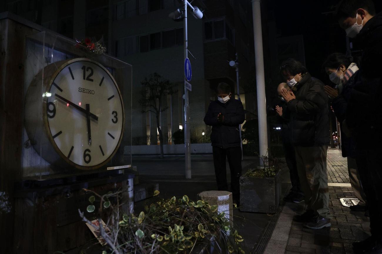 阪神大震災から27年となり、発生時刻で止まったままの大時計を囲み黙とうする人たち（共同）
