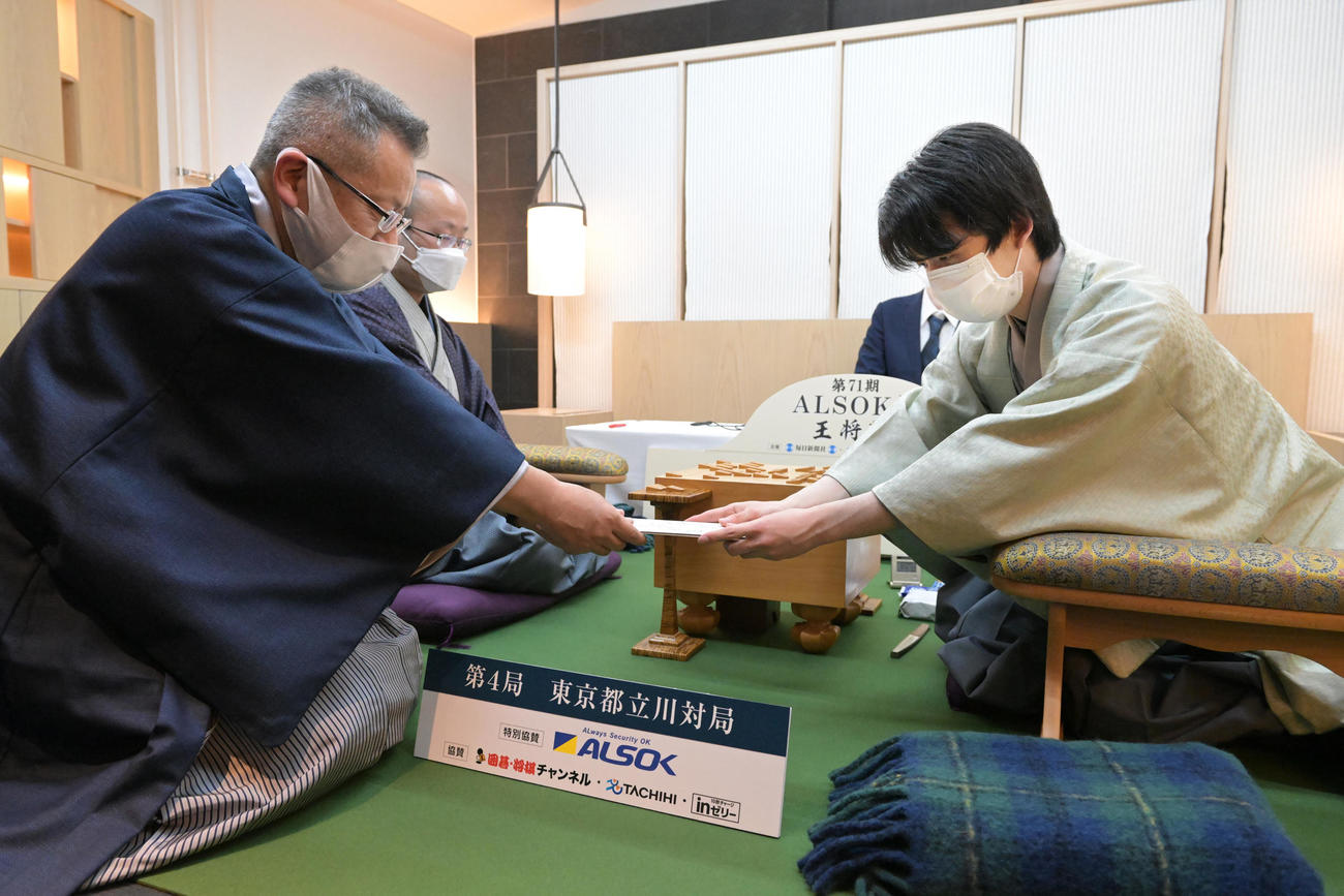 第71期ALSOK杯王将戦七番勝負第4局で、立会の中村修九段（左）に封じ手を渡す挑戦者の藤井聡太竜王（右）。左から2人目は渡辺明王将（代表撮影）