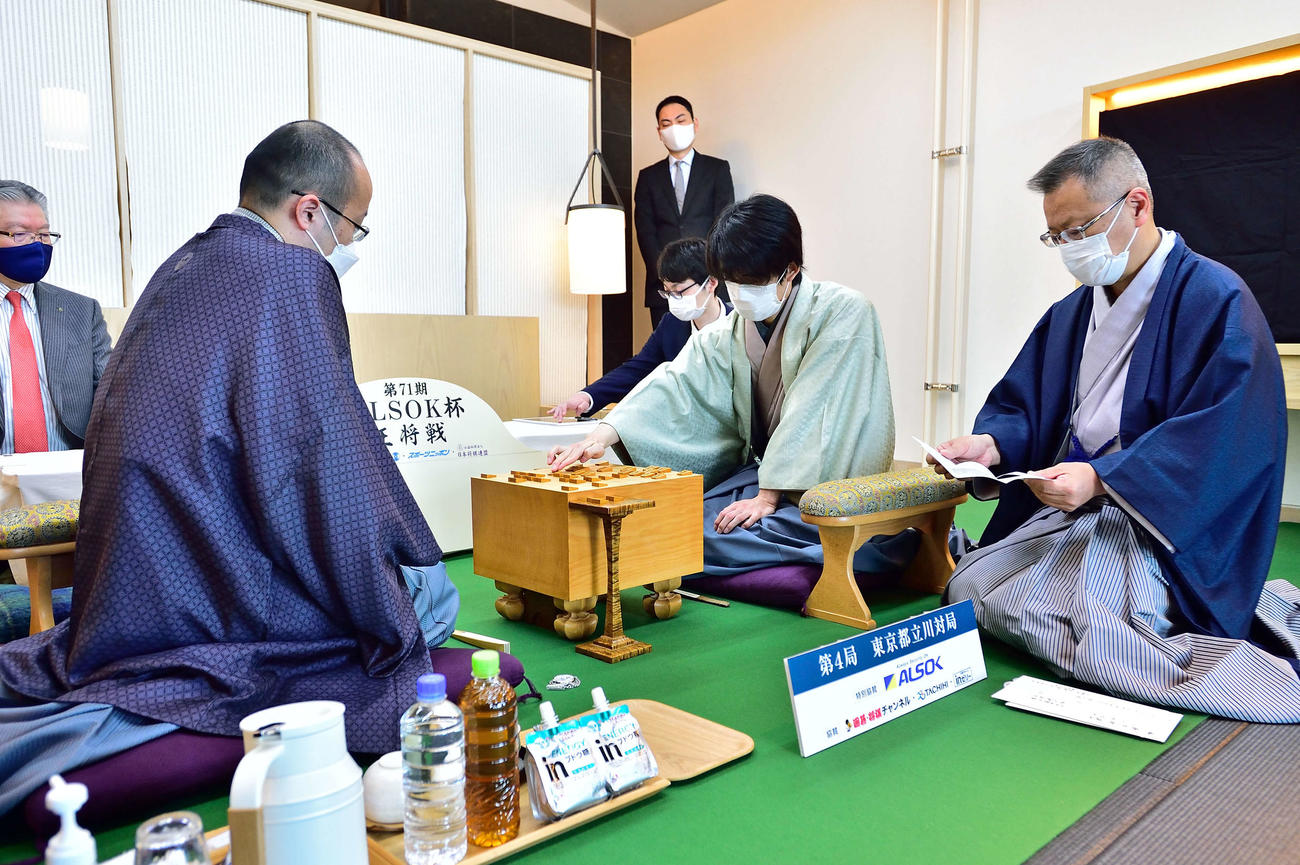 立会人の中村修九段（右）が読み上げた封じ手を藤井聡太竜王（中央）が指して対局再開（左は渡辺明王将、日本将棋連盟提供）