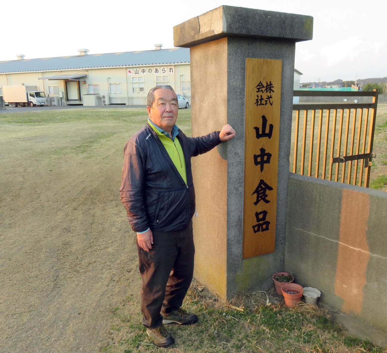社名を書き直した看板の脇に立つ「山中食品」の山中武夫社長（撮影・鎌田直秀）
