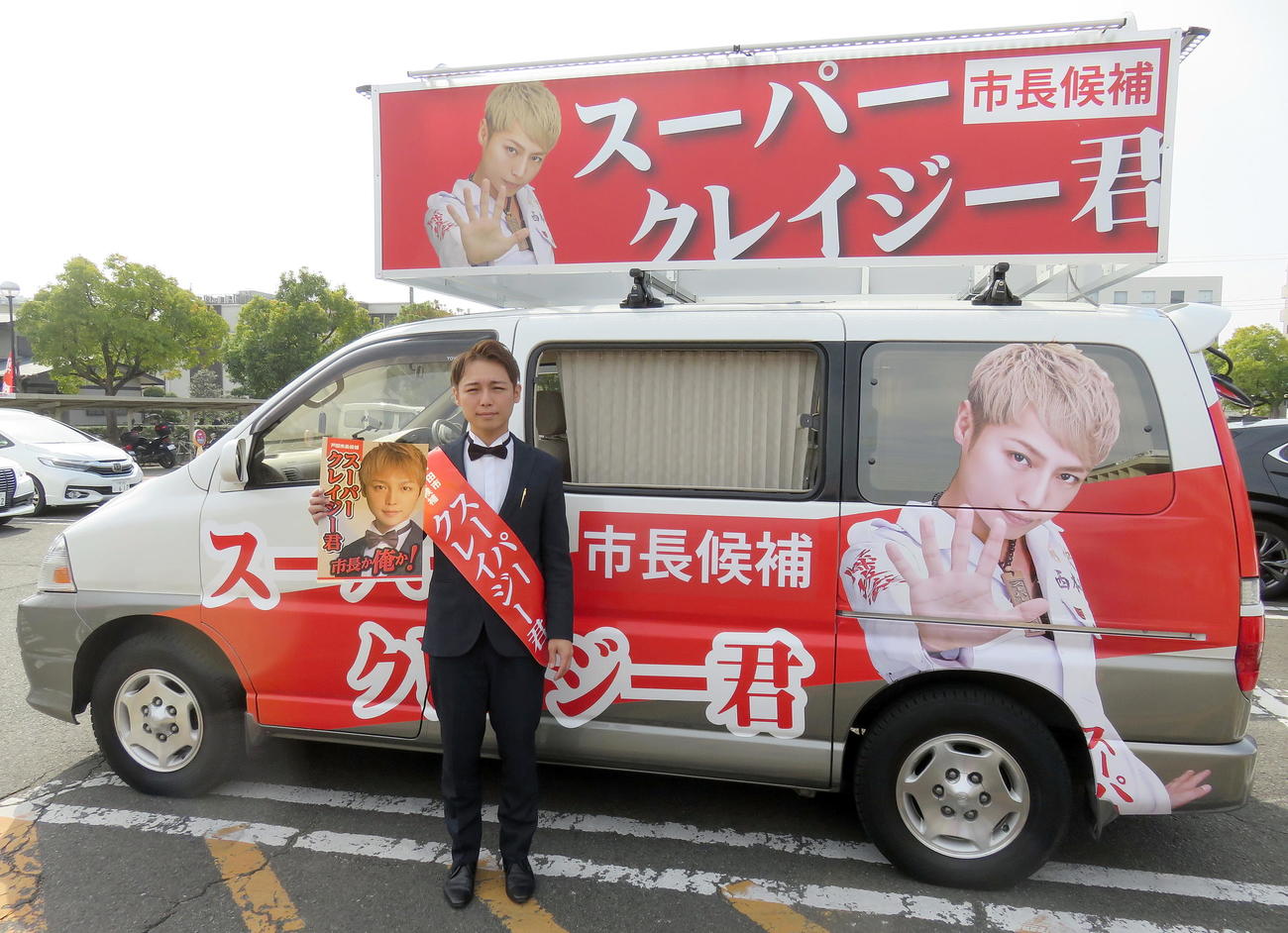 戸田市長選用の選挙カーの前でポスターも披露するスーパークレイジー君氏（撮影・鎌田直秀）