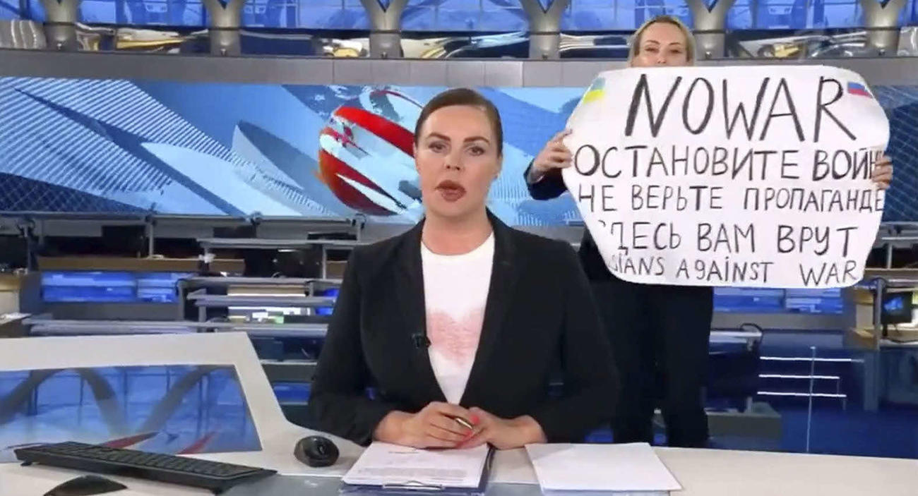 14日、ロシアのテレビの生放送中、キャスターの背後で「戦争反対」などと書いた紙を掲げるオフシャンニコワさん（ウクライナのポドリャク大統領府長官顧問のツイッターより、共同）