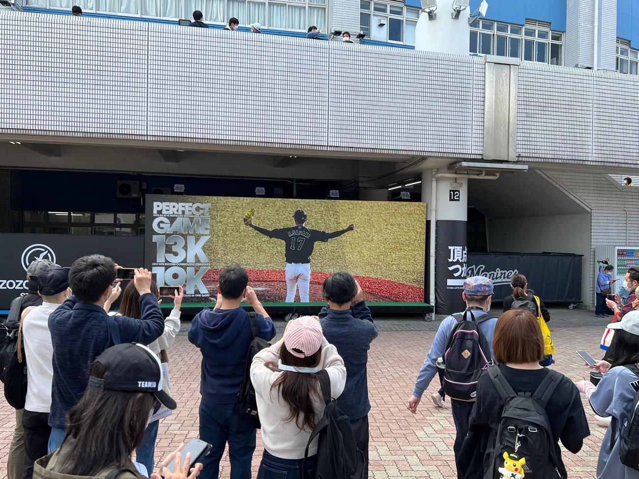 ZOZOマリンに設置されたロッテ佐々木朗の完全試合記念ボードで写真撮影するファン（撮影・金子真仁）