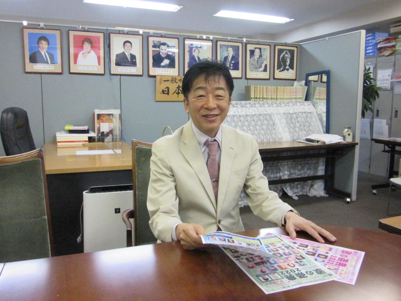 日本歌手協会歴代会長の写真の前で60周年について語る合田道人理事長