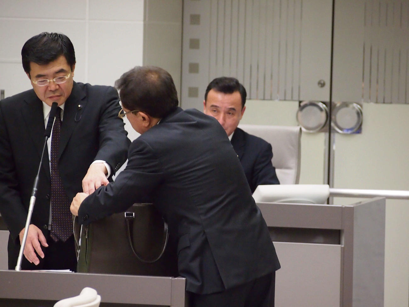 都議会総務委員会集中審議　徳田氏から受け取った5000万円を入れたというかばんに、5000万円の札束と同じ大きさの紙袋を入れようとする猪瀬直樹氏（右）＝2013年12月16日