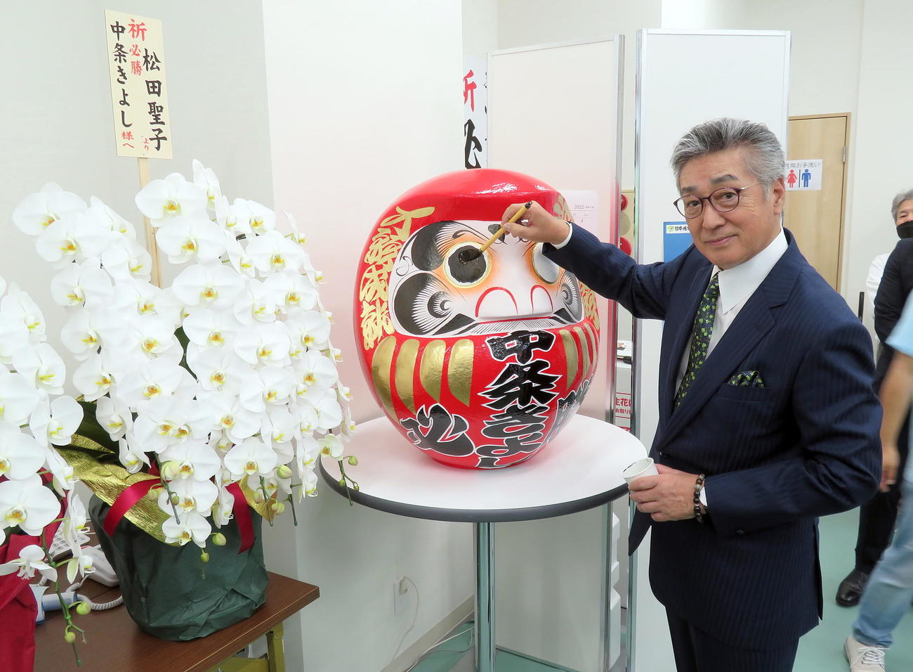 松田聖子から贈られた花の前で必勝だるまに目入れを行う中条きよし氏（撮影・鎌田直秀）