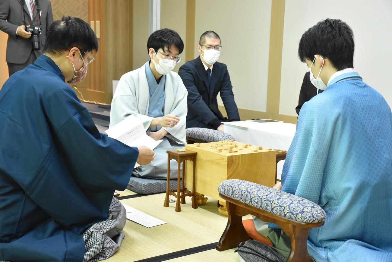 王位戦7番勝負第1局2日目、豊島将之九段（左）の封じ手を読み上げる立会人の小林健二九段（中央）（日本将棋連盟提供）