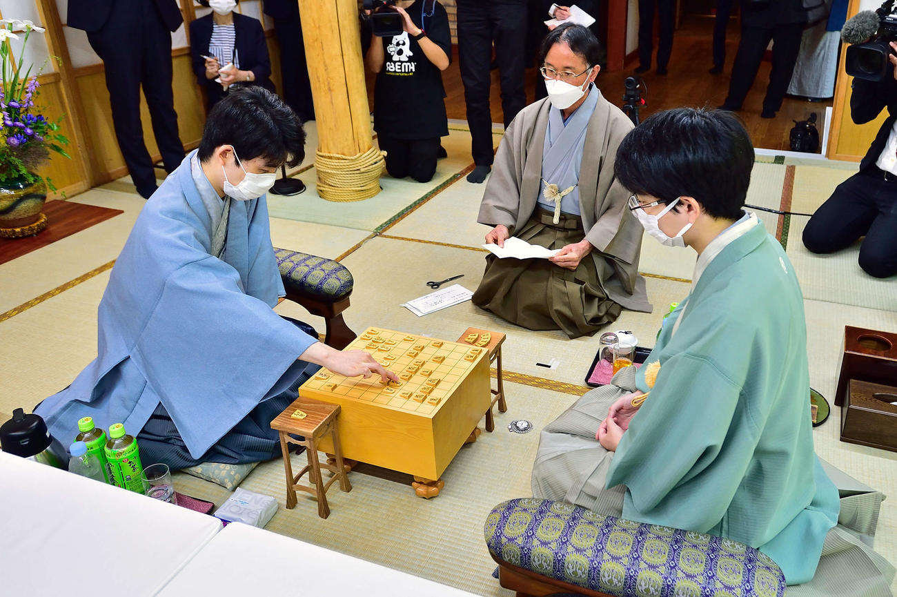 藤井聡太王位（左）の封じ手が立会人の深浦康市九段（中央）によって読み上げられ、対局再開（右は豊島将之九段、日本将棋連盟提供）