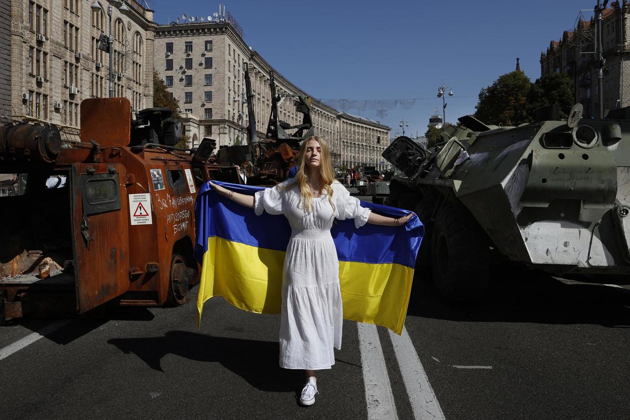 ロシアの侵攻から半年の節目と重なるウクライナの独立記念日を迎え、ロシア軍車両などが展示された首都キーウ中心部の大通りで、国旗を掲げて歩く女性（共同）