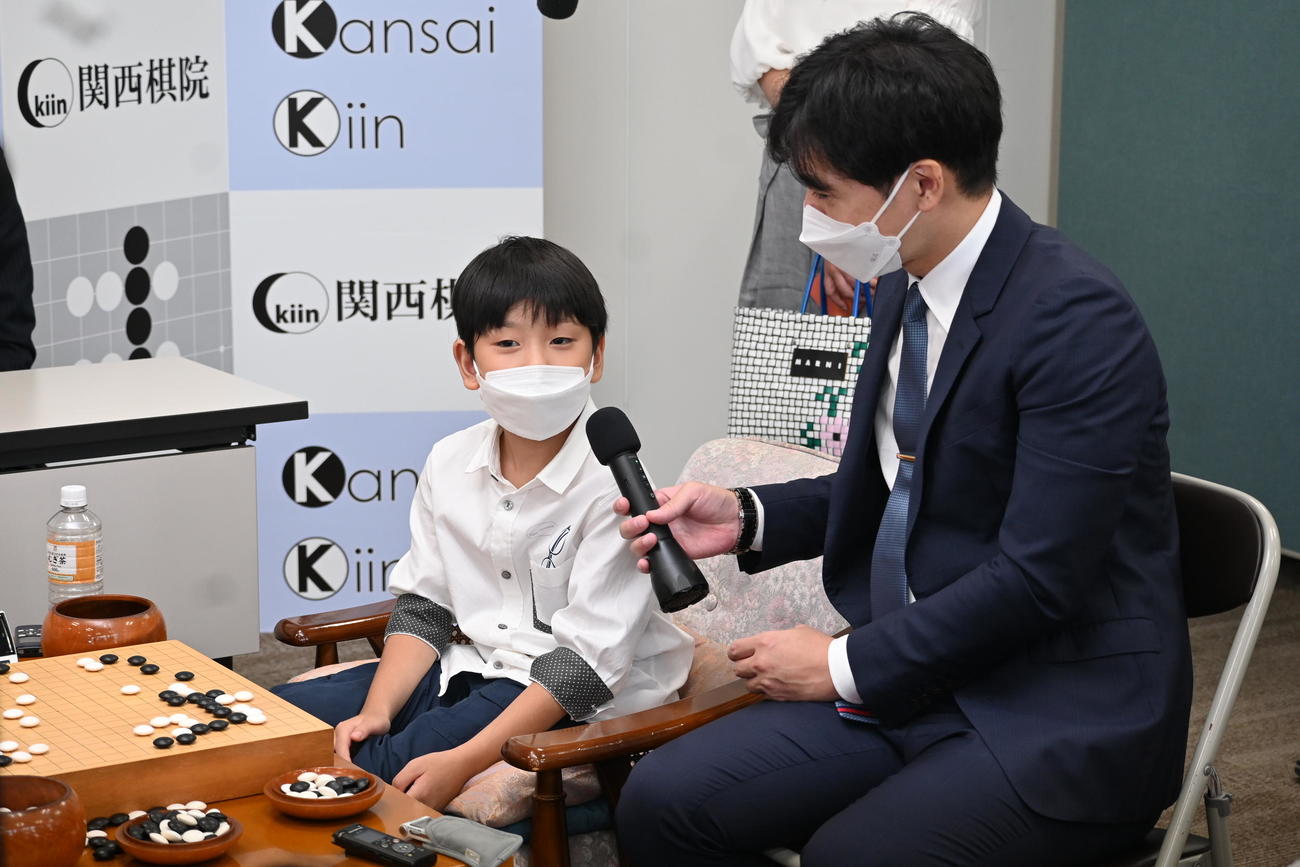 記念対局が終わり、師匠の星川拓海五段（右）にマイクを持ってもらい、質問にうなずく藤田怜央初段（撮影・松浦隆司）