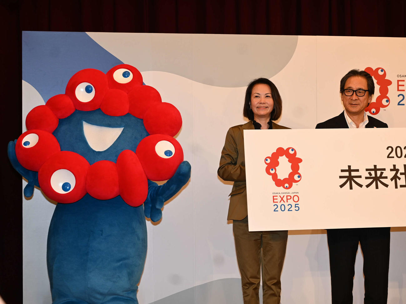 2025年の大阪・関西万博の公式キャラクター「ミャクミャク」（左）は写真撮影で代表者らをエスコート（撮影・松浦隆司）