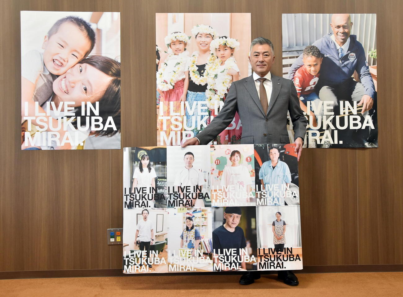市民をモデルにした「I LIVE IN TSUKUBAMIRAI」ポスターのパネルを持つ小田川浩市長