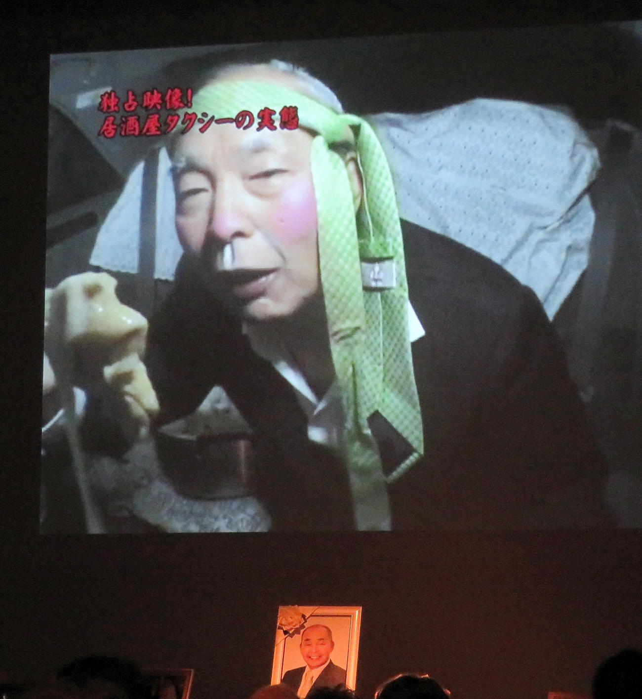 お別れの会で流れた「ザ・ニュースペーパー」渡部又兵衛さんが鈴木ムネオ議員を演じる映像（撮影・鎌田直秀）