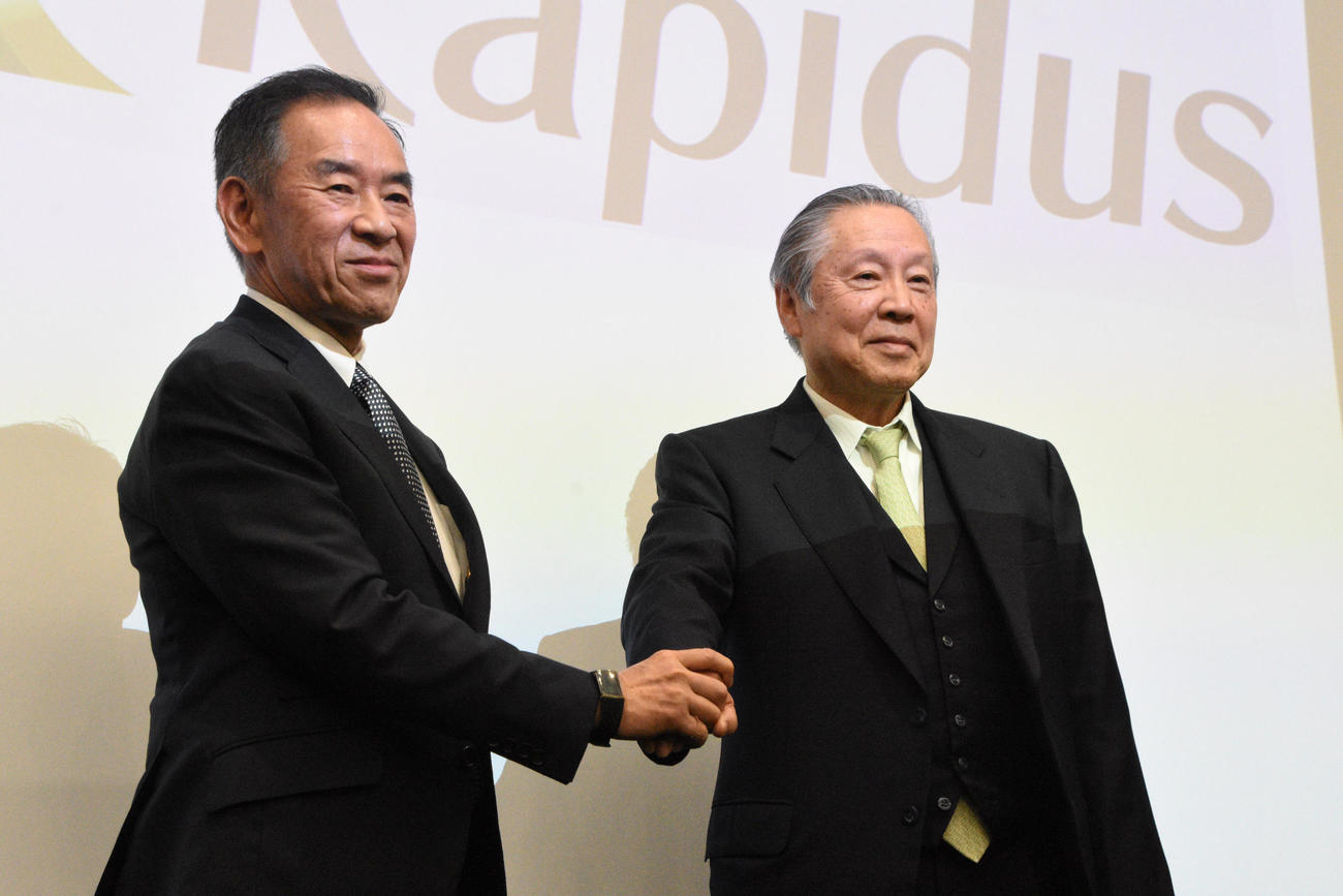 11月11日、日本の主要8社が設立した半導体の新会社「Rapidus」（ラピダス）の記者会見で握手を交わす小池淳義社長（左）と東哲郎会長（朝日新聞）