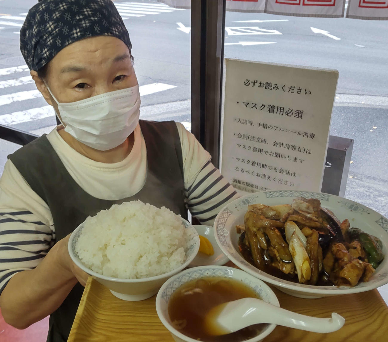 ごはん大盛りのナスと豚肉の黒味噌炒め定食を持つ野村信子さんは「みなさん、よく食べますよ」とニッコリ（撮影・寺沢卓）