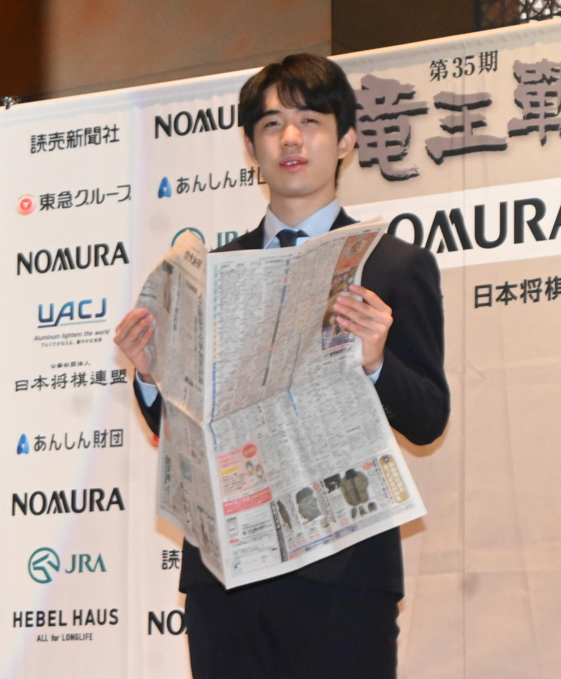 竜王初防衛の一夜明け会見で初防衛を報じる新聞を見る藤井聡太竜王（撮影・松浦隆司）