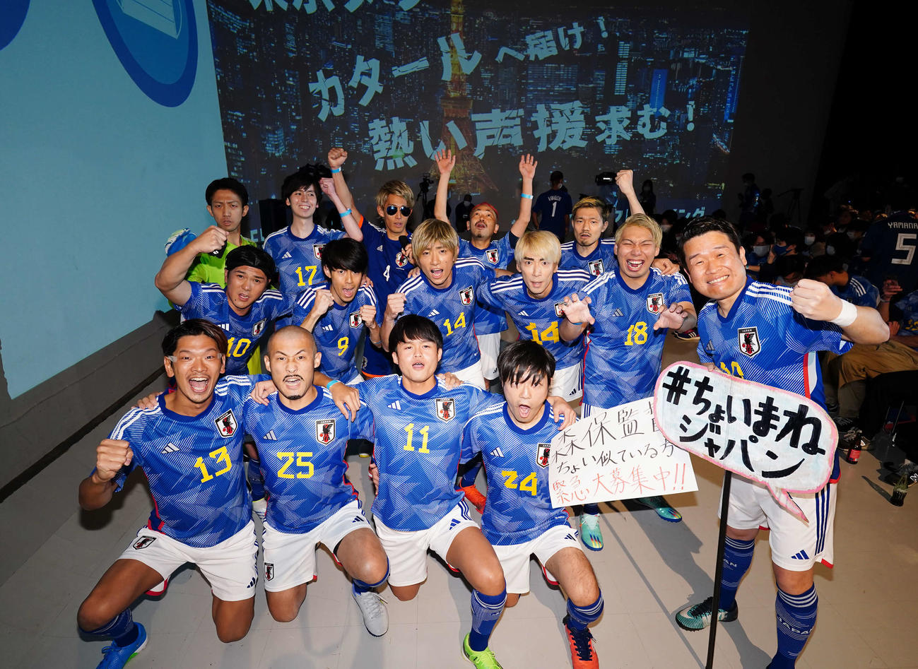 PV会場で盛り上がる「＃ちょいまねジャパン」のメンバー。前列左からDF守田、FW前田、MF久保、MF相馬、DF酒井、中列左からMF南野、MF三笘、MF伊東が2人、FW浅野、後列左からGK権田、MF田中、本田圭佑氏、DF長友、DF守田にそれぞれ寄せている人たち（撮影・菅敏）