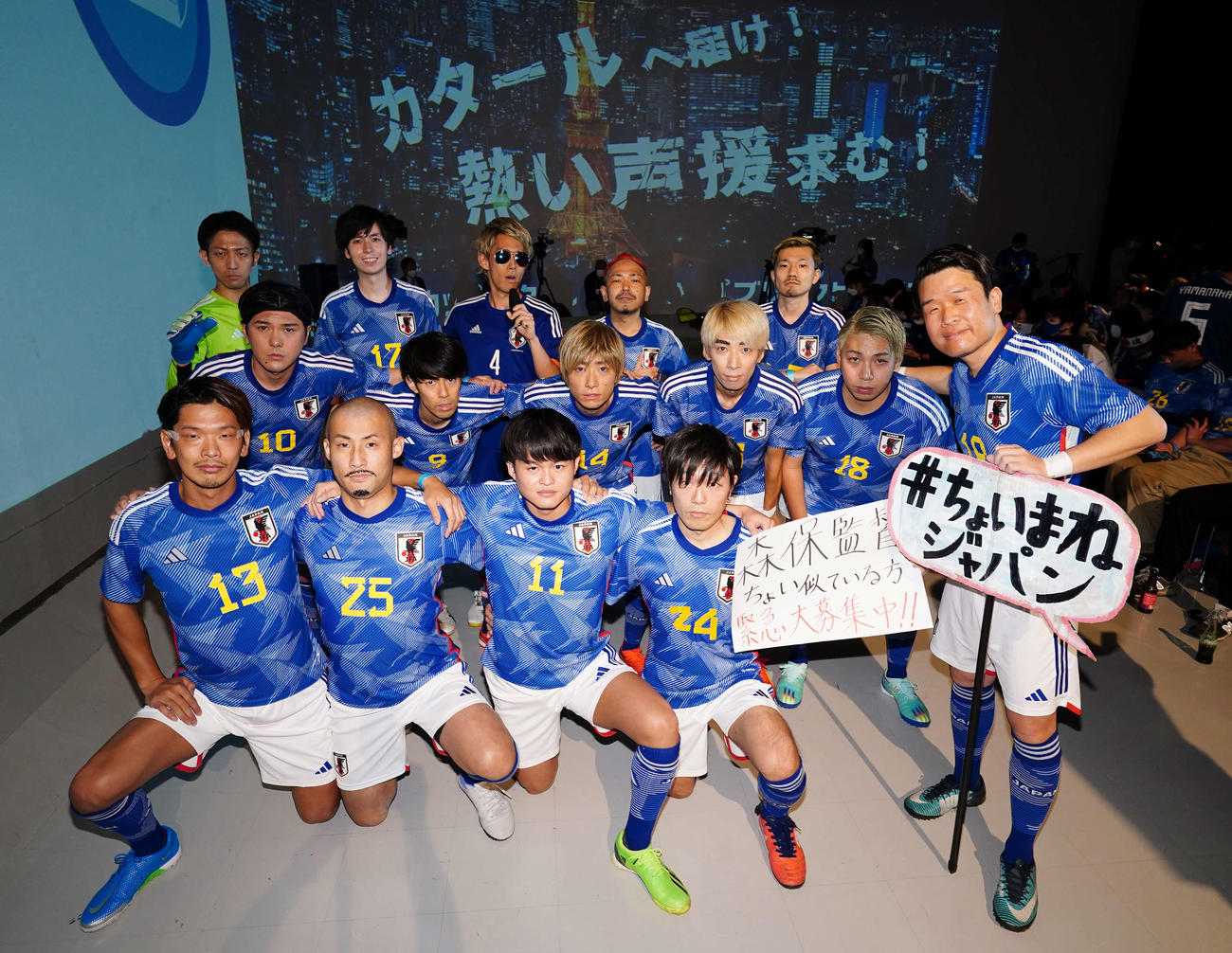 PV会場で盛り上がる「＃ちょいまねジャパン」のメンバー。前列左からMF守田、FW前田、MF久保、MF相馬、DF酒井、中列左からMF南野、MF三笘、MF伊東が2人、FW浅野、後列左からGK権田、MF田中、本田圭佑氏、DF長友、MF守田にそれぞれ寄せている人たち
