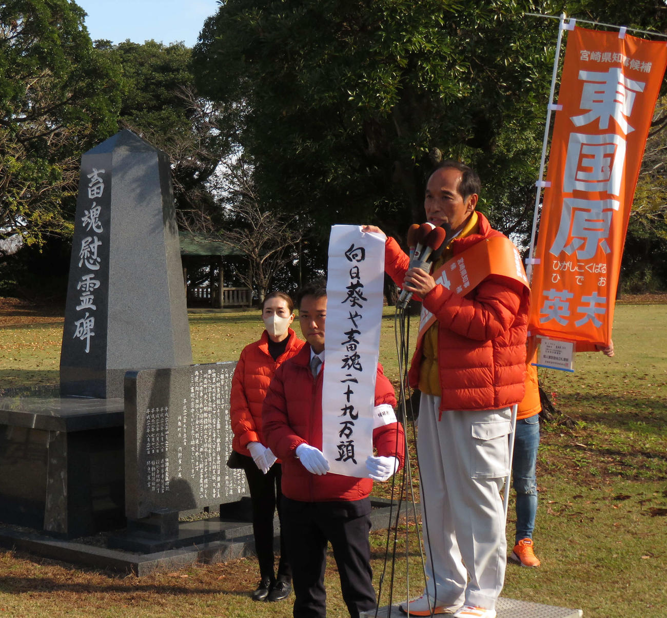 宮崎県知事選に立候補した東国原英夫前知事は川南町の畜魂慰霊碑前で「向日葵や畜魂二十九万頭」という俳句を披露。俳句を持つのは長男加藤守さん、後方のマスクの女性は妻春香さん（撮影・寺沢卓）
