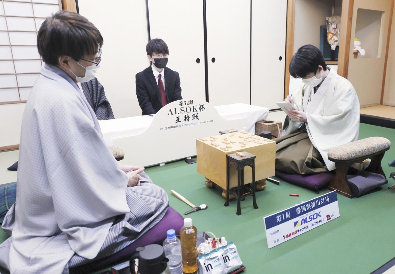 第72期王将戦7番勝負第1局の第1日、封じ手の入った封筒に署名する藤井聡太王将。左は挑戦者の羽生善治九段（代表撮影）