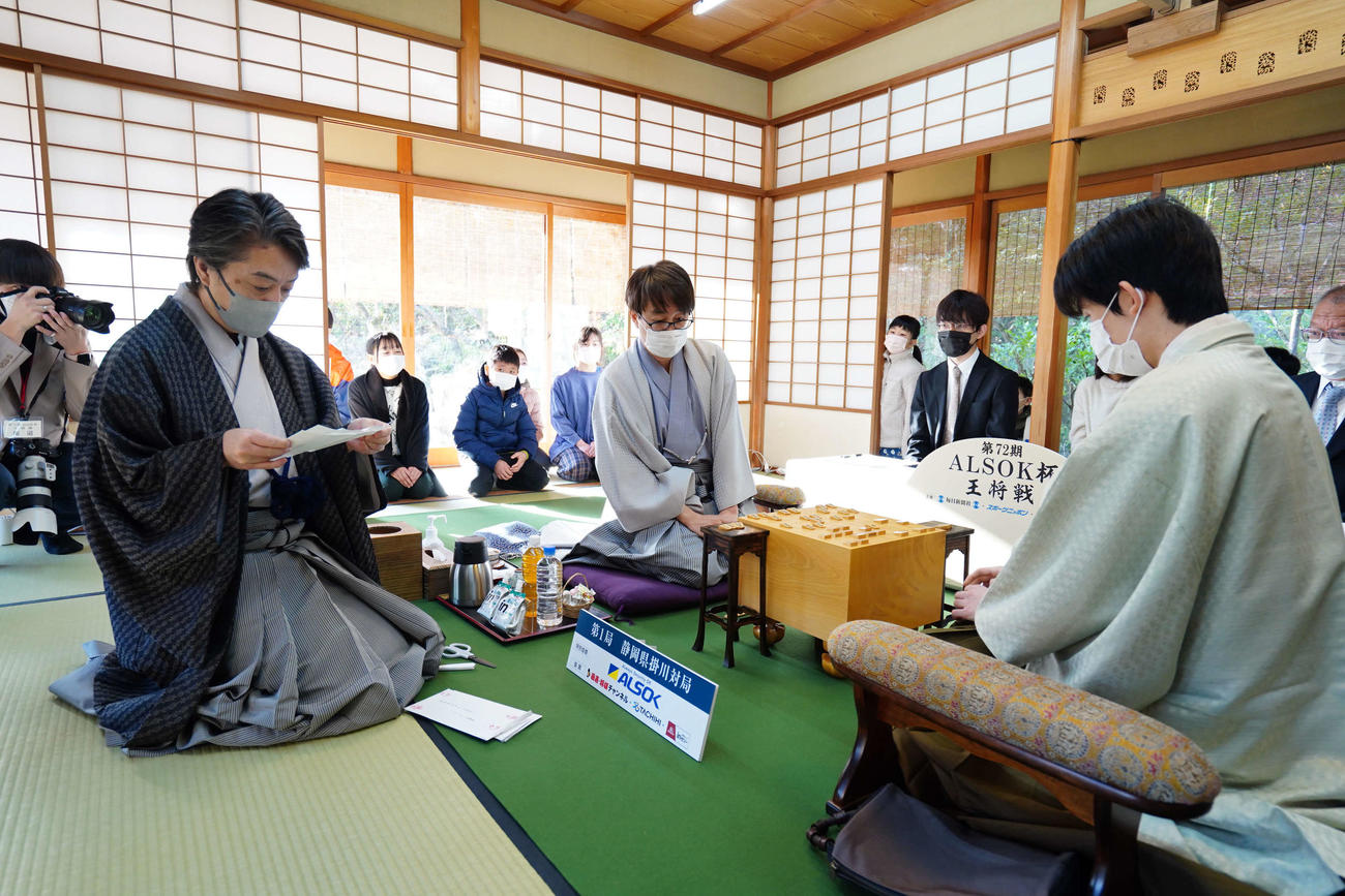 立会人の久保利明九段（左）が開封した封じ手に耳を傾ける羽生善治九段（中央）と藤井聡太王将（右、日本将棋連盟提供）
