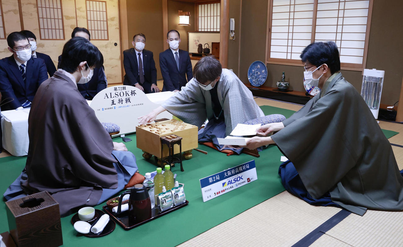立会の谷川浩司十七世名人（右）が開封した封じ手を指す挑戦者の羽生善治九段（中央）。左は藤井聡太王将（代表撮影）