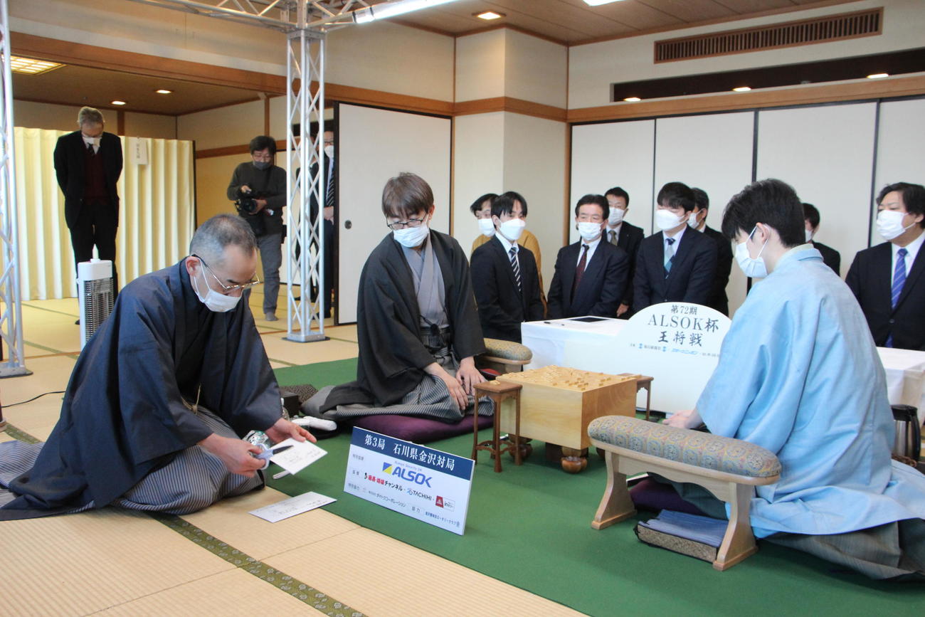立会人の島朗九段（左）が開封した封じ手を確認する羽生善治九段（中央）、藤井聡太王将（日本将棋連盟提供）