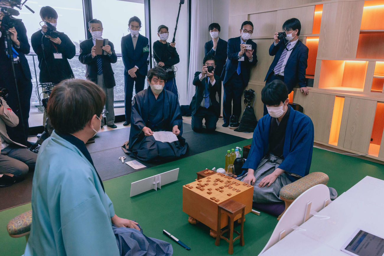 羽生善治九段（左）が藤井聡太王将（右）に挑戦する王将戦第4局は立会人の森内俊之九段（中央）が封じ手を開いて2日目がスタート（日本将棋連盟提供）