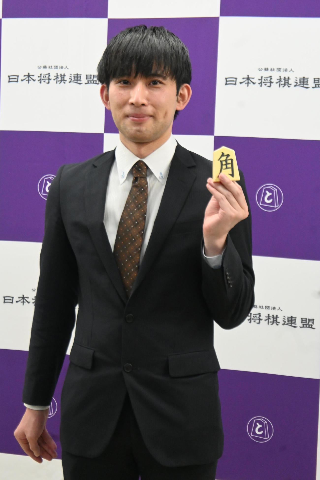 終局後、好きな駒「角」を持ち写真撮影に応じる小山怜央アマ（日本将棋連盟提供）
