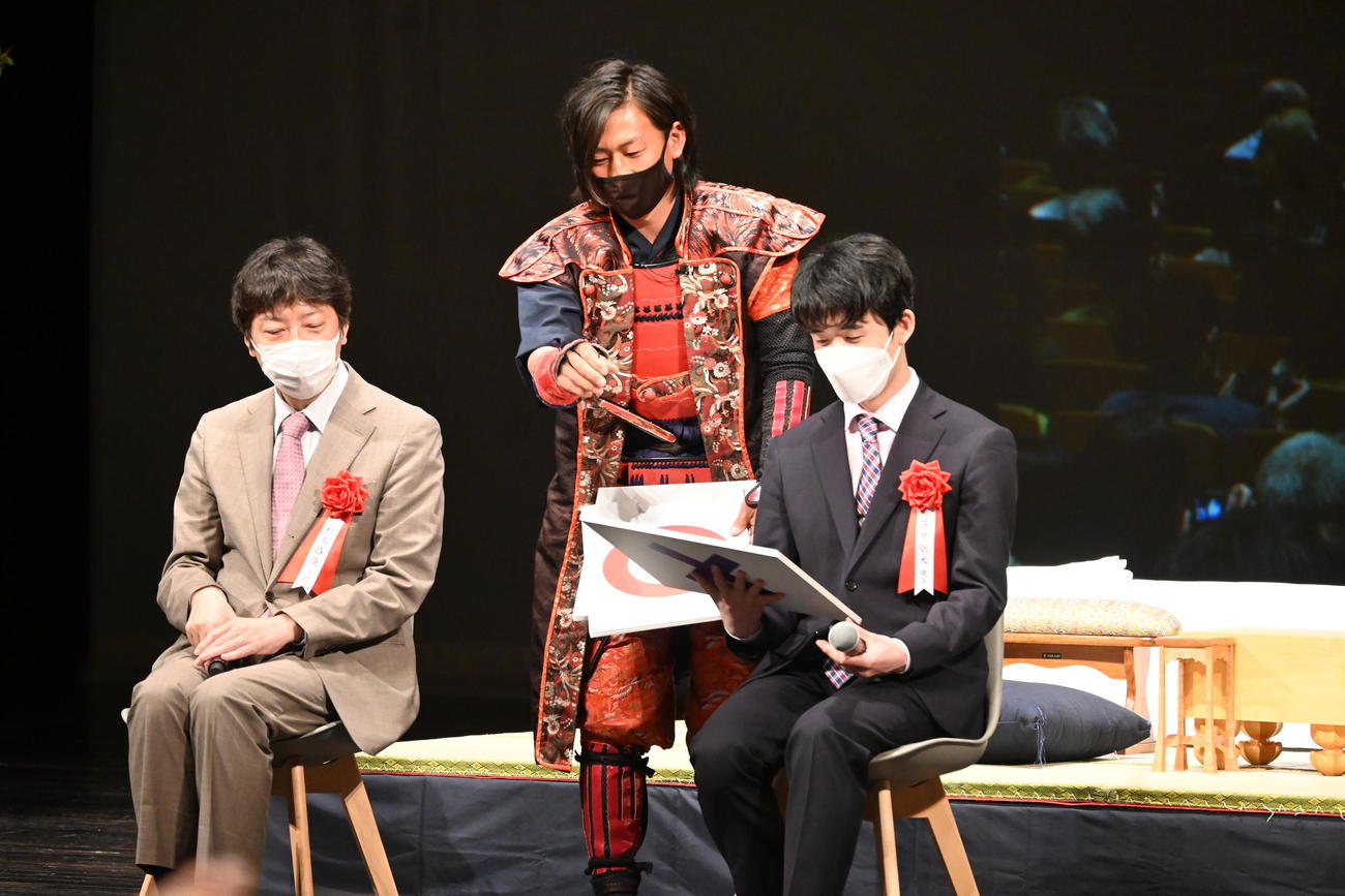 グレート家康公「葵」武将隊の井伊直政（中央）から「家康クイズ」に使うボードを受け取る藤井聡太竜王（右）。左は師匠の杉本昌隆八段（撮影・松浦隆司）