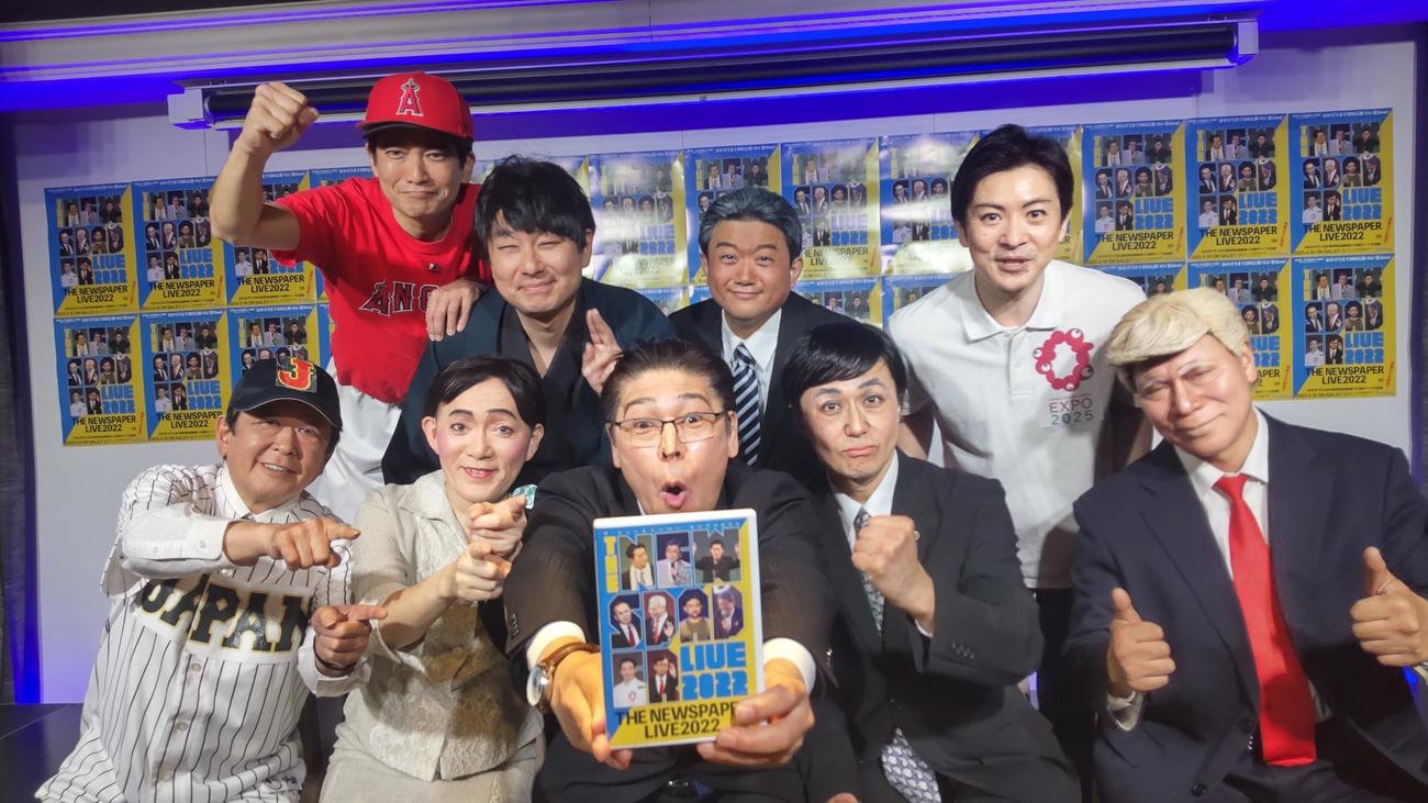 ザ・ニュースペーパーのメンバー9人。前列左から竹内康明（クリヤマ監督）、山本天心（えりあるふぃや）、新作DVDを突き出す浜田太一（キシダ総理）、福本ヒデ（吉田シンジ）、松下あきら（とらんぷ前大統領）、後列左から石坂タケシ（大谷ショウヘイ）、土谷ひろし（藤井ソウタ）、田中カツノリ（ババ代表）、田中学（ヨシムラ府知事）（撮影・寺沢卓）