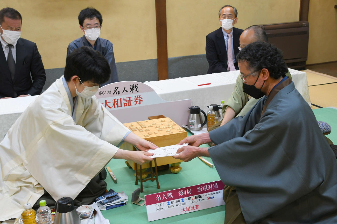 第81期名人戦7番勝負第4局1日目を終え、封じ手の封筒を立会人の深浦康市九段（右）に手渡す藤井聡太竜王（日本将棋連盟提供）
